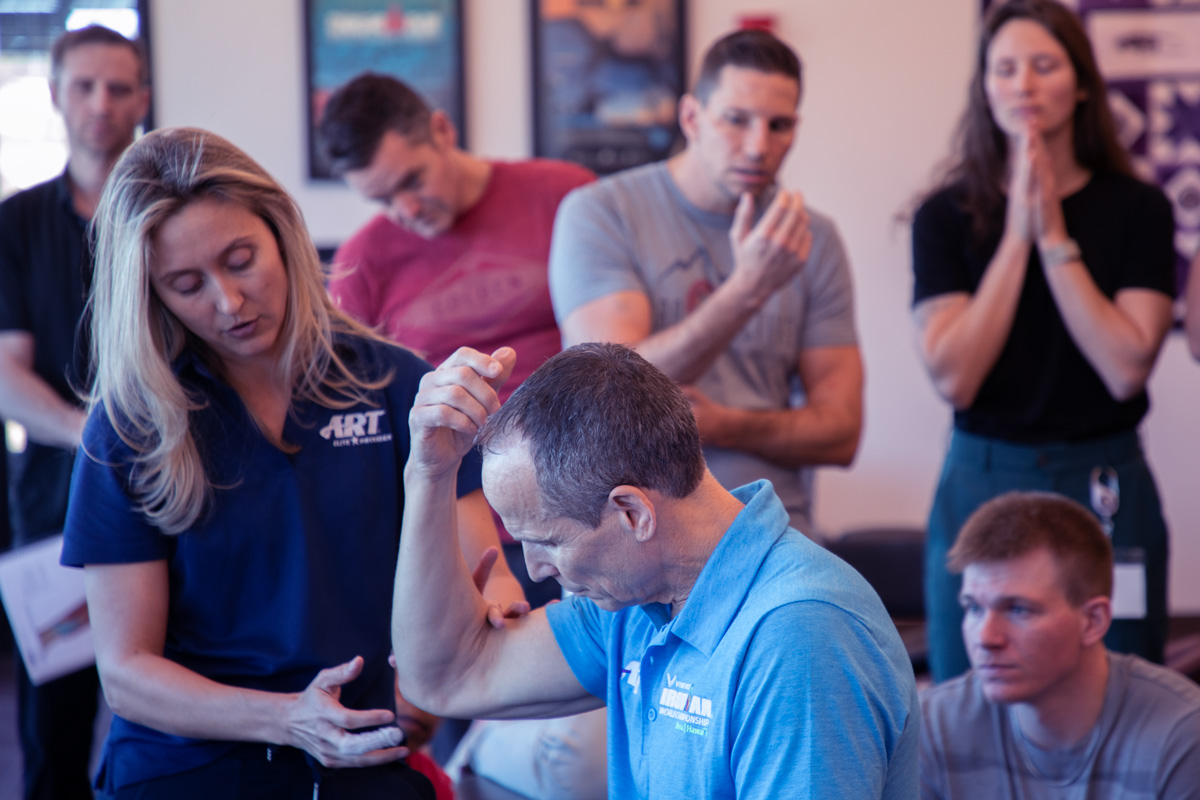 Photo of a female ART instructor demonstrating an ART protocol on the elbow of a male ART instructor as providers and students watch and practice on themselves.